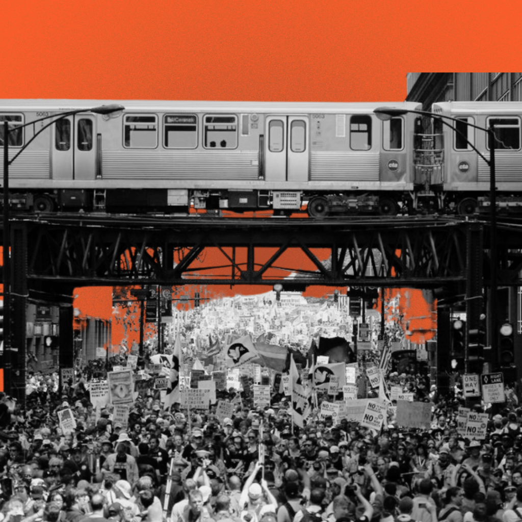 A large protest crowd with signs and banners beneath an elevated train on a steel bridge.