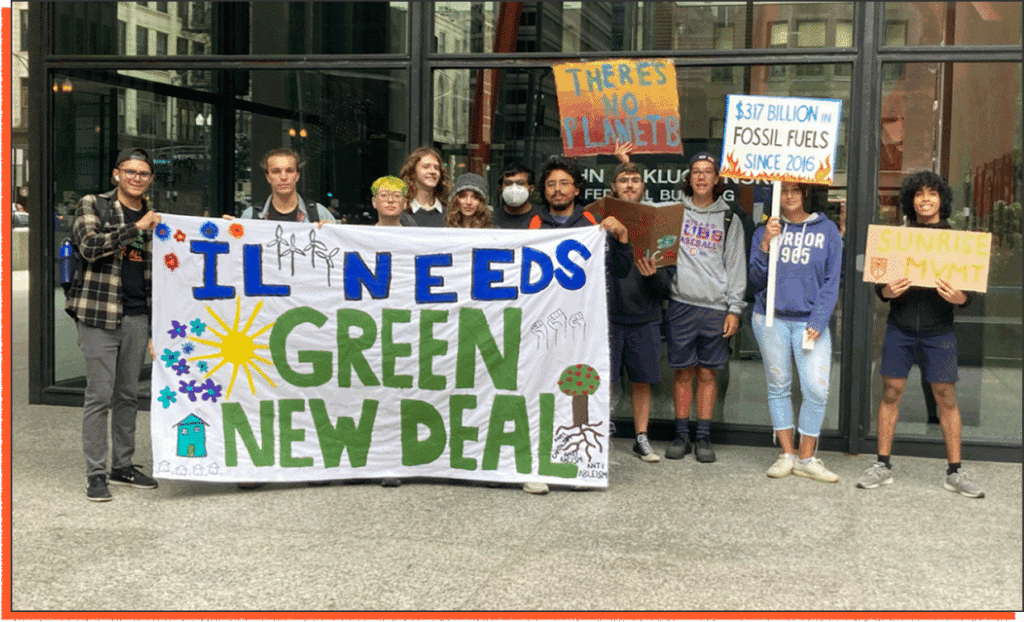 A group of people stand in front of a building holding signs advocating for climate action and a Green New Deal in Illinois.