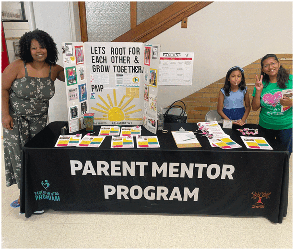 Three people stand behind a table with Parent Mentor Program signage, brochures, and a display board promoting community support and collaboration.
