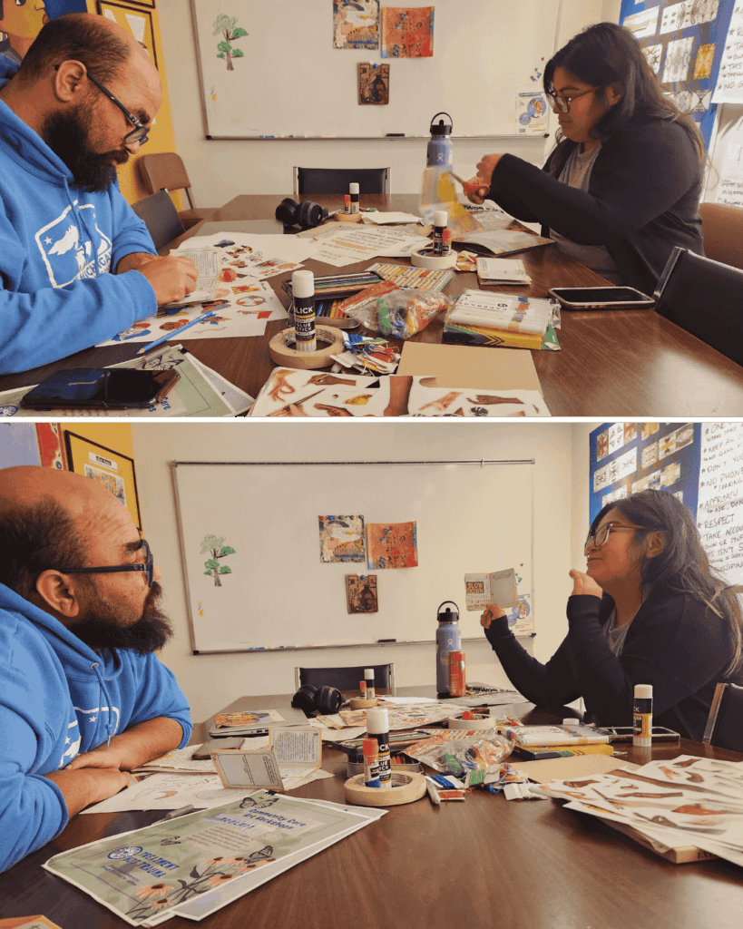 Two people sit across from each other at a table covered with craft supplies, working on arts and crafts projects in a classroom setting.
